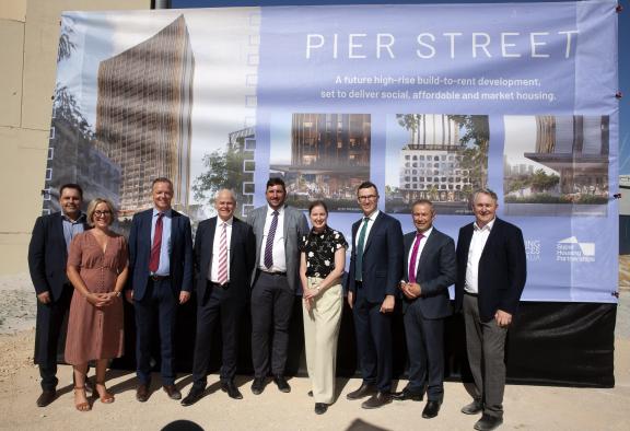 Delegates in front of a backdrop depicting artist impressions of the new Pier Street development