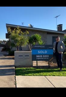 Young man standing outside his first home smiling next to SOLD sign